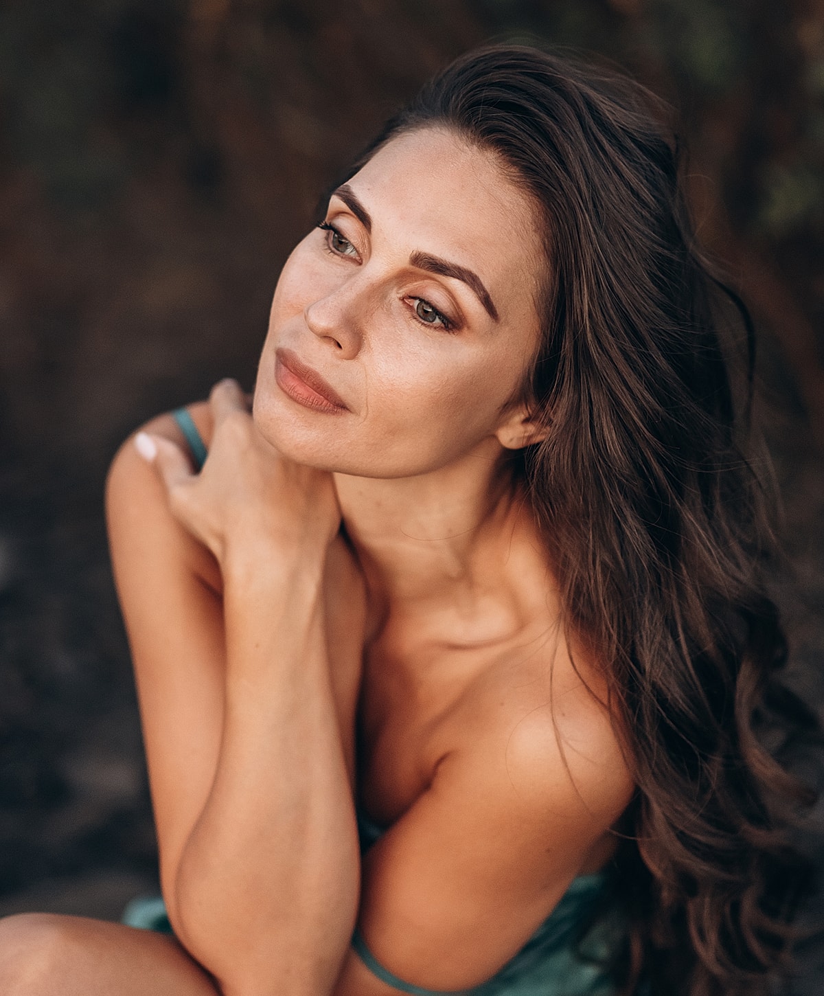Woman with long hair, thoughtful expression, natural setting.