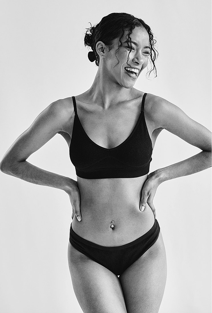 Smiling model in black lingerie against neutral background.