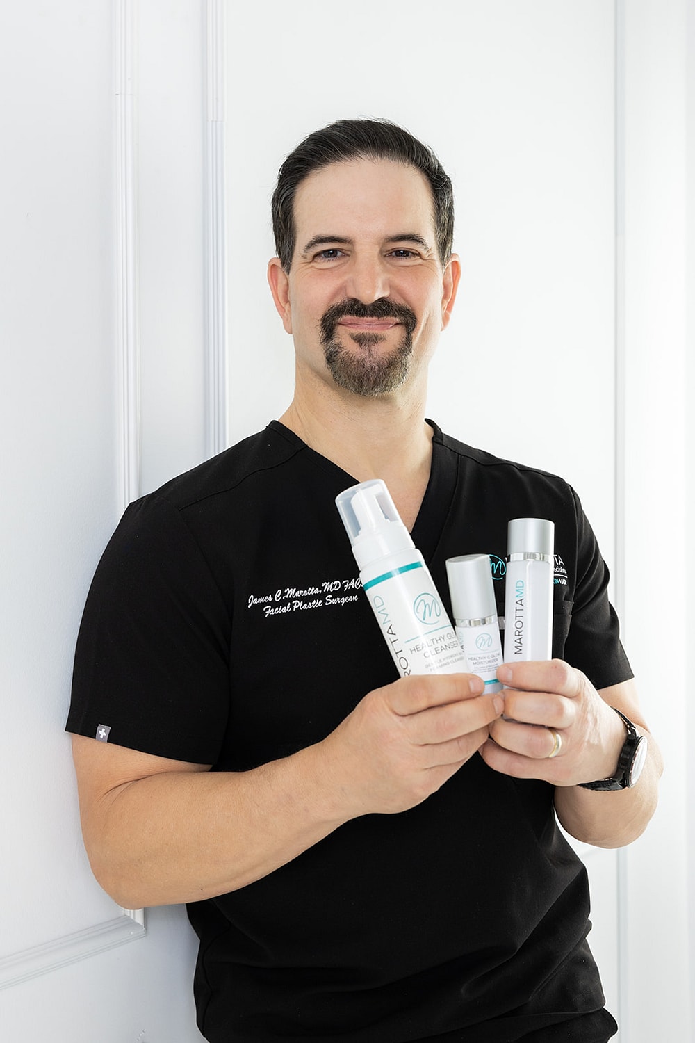 Doctor holding skincare products in clinic setting.