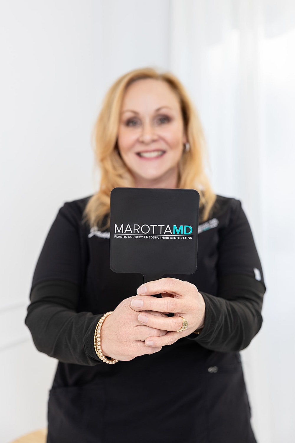 Woman holding mirror with Marotta MD branding.